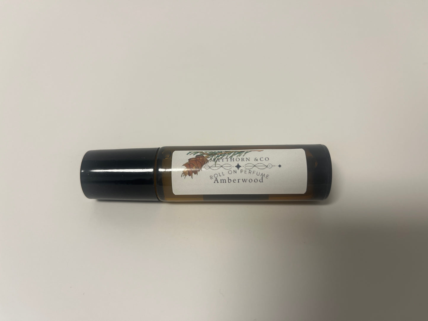 Maythorn & Co Amberwood roll-on perfume bottle with amber-colored liquid and sleek glass design.