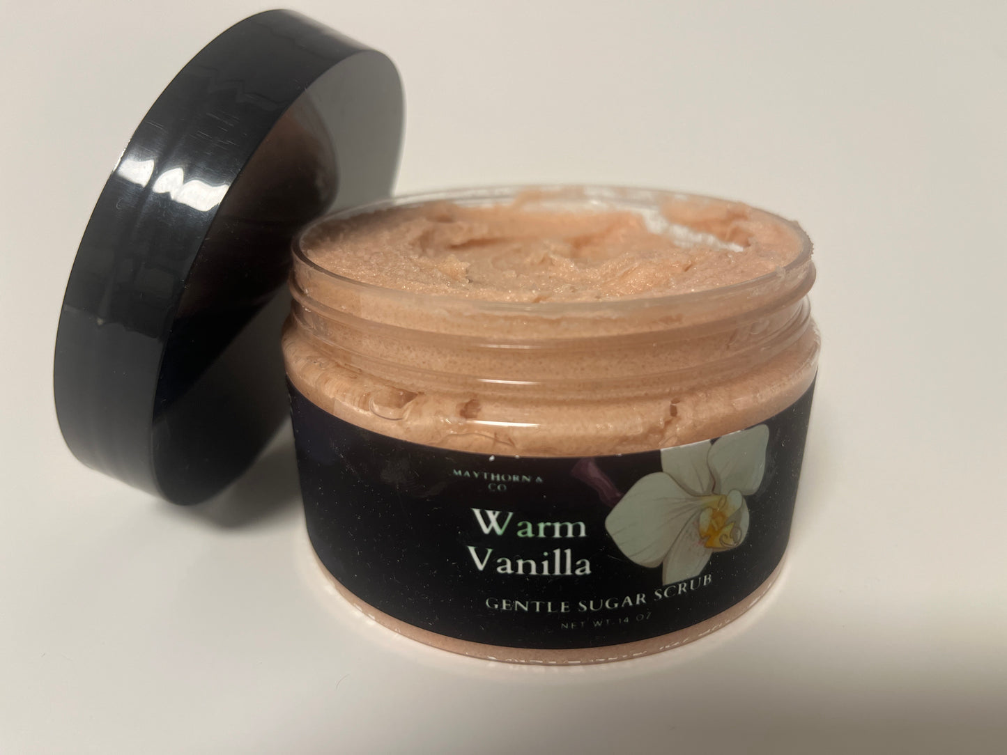Maythorn & Co Warm Vanilla Body Scrub with natural exfoliants and a creamy vanilla scent, displayed in a jar with a wooden scoop.